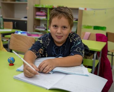 Smiling pupil writing in his notebook in class
