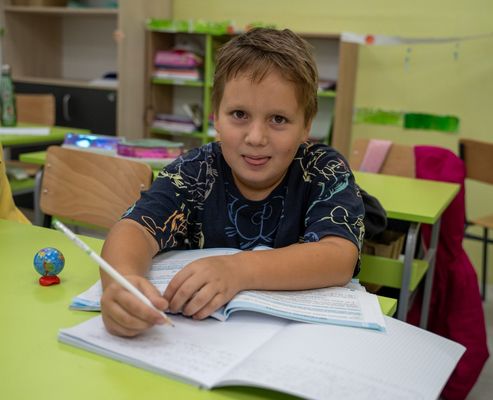 Smiling pupil writing in his notebook in class